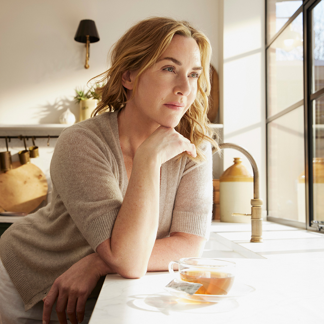 Närbild på Kate Winslet som tittar ut, har en kopp te med kollagenpulver från Oslo Skin Lab bredvid sig.