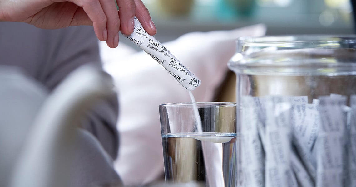 En närbild av en kvinnlig hand som häller upp en dagsdos av kollagenpulvret The Solution i ett glas.