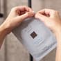 Händer som öppnar en förpackning av lyxiga ansiktsmasken Hydro Bomb från Oslo Skin Lab