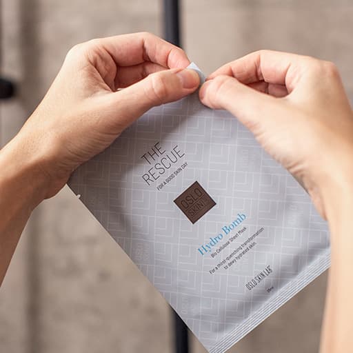 Händer som öppnar en förpackning av lyxiga ansiktsmasken Hydro Bomb från Oslo Skin Lab
